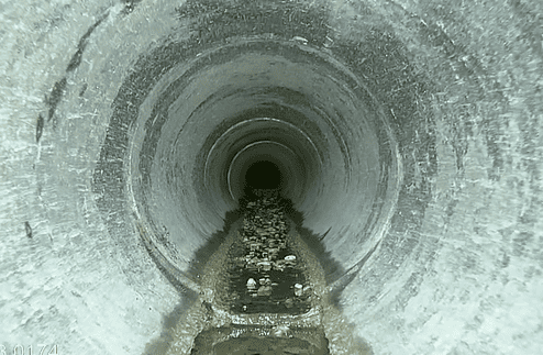 Blick in einen langen, runden Rohrkanal mit Wasser und Sedimentablagerungen am Boden.