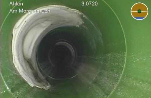 Blick ins Innere eines grünen Rohres, mit leichtem Wasserfluss und einer glatten, weißen Innenwand.