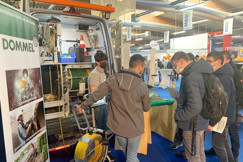 Menschen stehen am Stand eines Unternehmens und betrachten ein Fahrzeug mit technischem Equipment für Kanalinspektion.