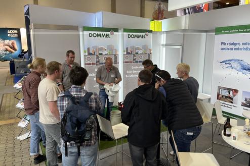 Gruppe von Menschen am Messestand von DOMMEL, die sich über Rohrsanierungsdienstleistungen informieren.