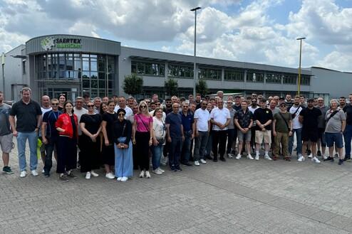 Gruppenfoto von über 50 Personen vor dem Eingang des Saertex-Werks unter einem bewölkten Himmel.