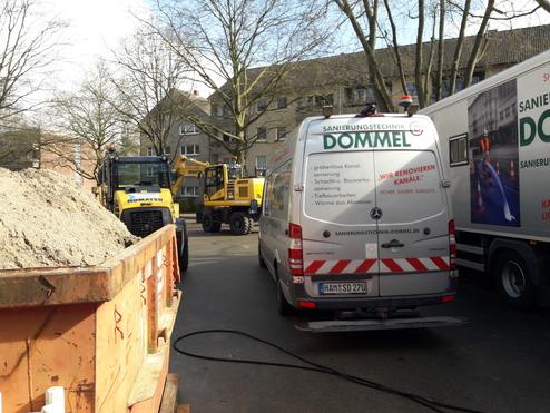 Baustelle mit einem Lkw, zwei Komatsu-Baumaschinen und einem Fahrzeug der Firma Dommel in einer urbanen Straße.