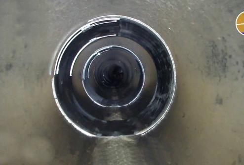 Innenansicht eines Rohres mit spiralförmigem Verlauf, das ins Dunkel führt. Die Wände sind glanzend und metallisch.