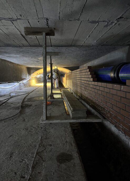 Arbeiter beim Verlegen von Ziegeln in einem abgedunkelten Tunnel mit Betonwänden und Holzplattform.