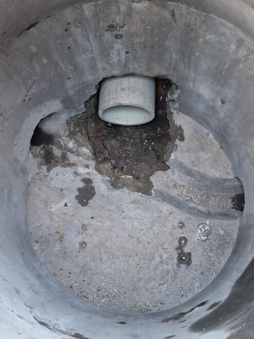 Runder, vertiefter Betonsockel mit einem Kunststoffrohr und losem Schmutz am Boden.