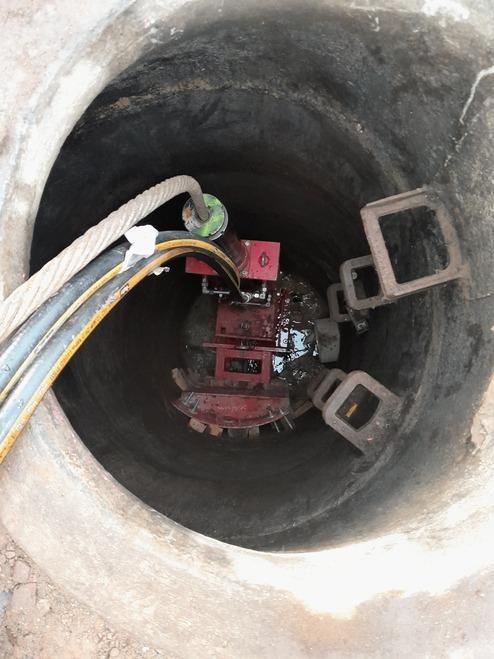 Blick in einen tiefen, runden Schacht mit einer roten Pumpe und angeschlossenen Schläuchen.