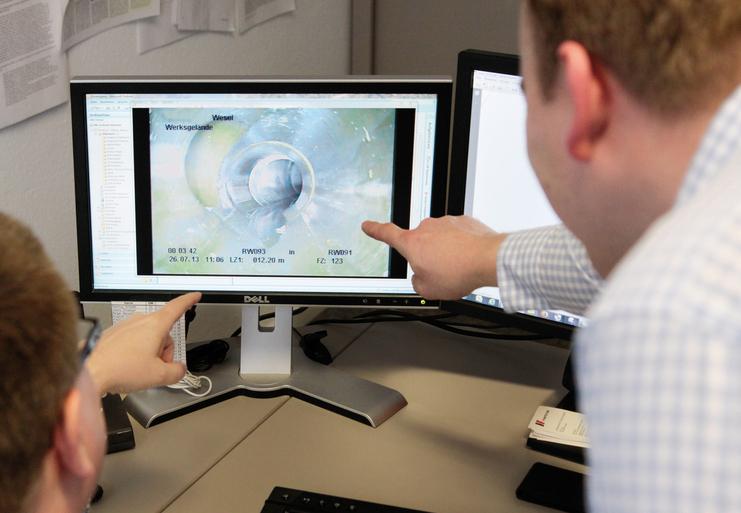 Zwei Personen beobachten einen Computerbildschirm mit einer Grafik und zeigen mit dem Finger auf spezifische Details.