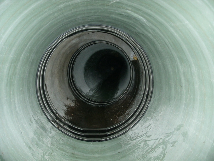 Blick in einen großen, runden, gläsernen Behälter mit glatten Wänden und dunklem Bodengrund.