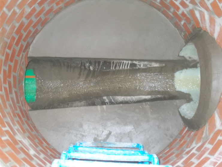 Blick in einen runden, gefliesten Schacht mit einem geraden Rohr und sichtbarem Wasserfluss.