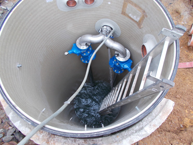 Blick in einen großen Zylinder mit grüner Flüssigkeit, zwei blauen Pumpen und einer Metallleiter.