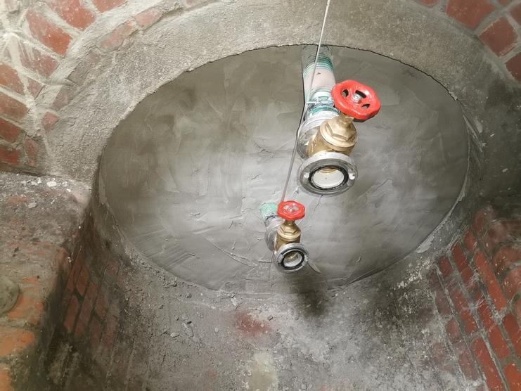 Zwei Wasserhähne mit roten Griffen in einem kreisförmigen, verputzten Raum mit Ziegelwänden.