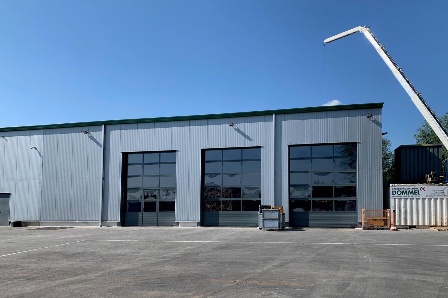 Blick auf ein graues Lagergebäude mit großen Fenstern und einem Kran, der über dem Dach positioniert ist.
