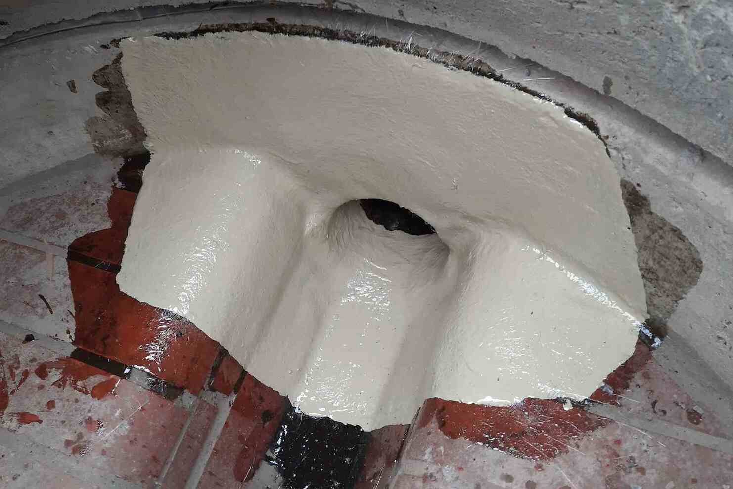 Reparierte Innenfläche mit frischer, glänzender Beschichtung und sichtbarem Wasserablauf auf einem gefliesten Boden.