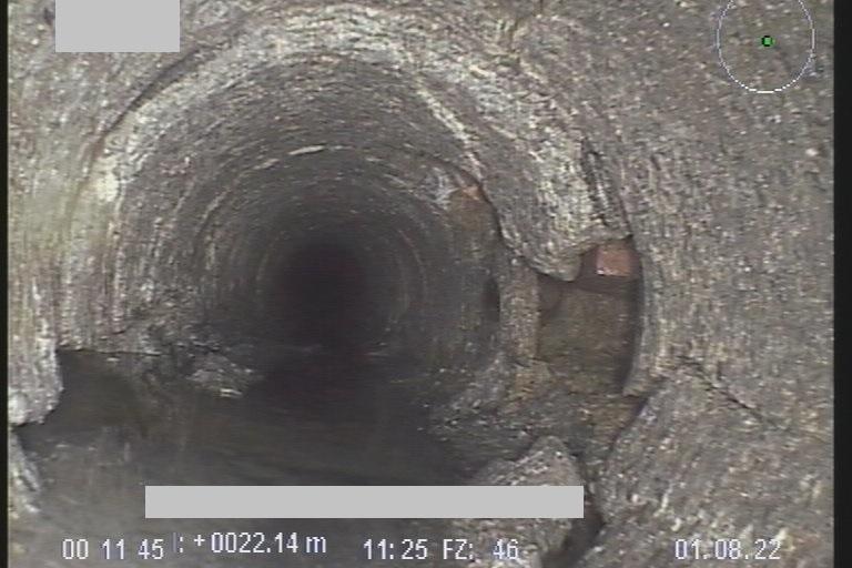 Blick in ein dunkles Abwasserohr mit Wasseransammlung und rauer Innenoberfläche.