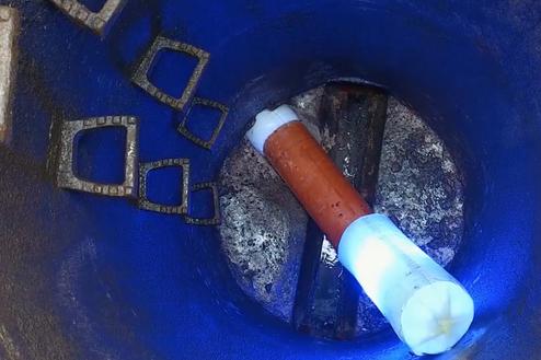 Blick in einen blauen Beh&auml;lter mit einem orangefarbenen Rohr und mehreren quadratischen Metallst&uuml;cken am Boden.