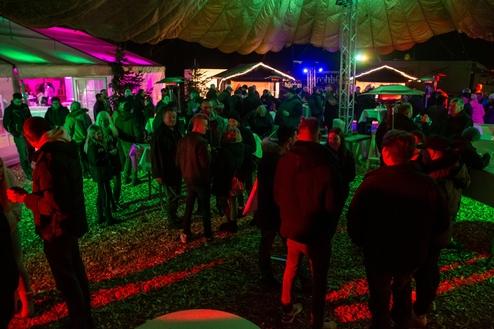Menschenmenge bei Nacht auf einer festlich beleuchteten Veranstaltung unter einem Zelt mit grünen und roten Lichtern.