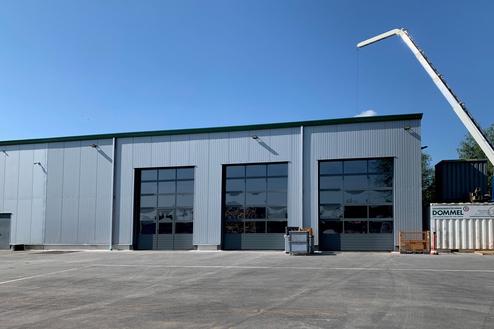 Blick auf ein graues Lagergebäude mit großen Fenstern und einem Kran, der über dem Dach positioniert ist.