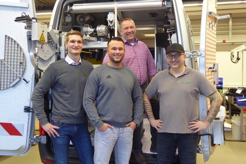 Vier Personen stehen vor einem offenen Lieferwagen, der mit technischer Ausrüstung ausgestattet ist.