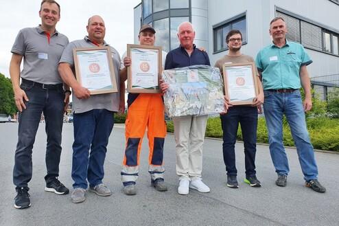 Gruppenfoto von sechs Männern mit Urkunden für langjährige Betriebszugehörigkeit vor einem Firmengebäude.
