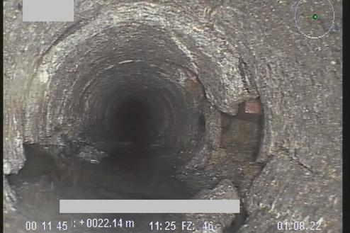 Blick in ein dunkles Abwasserohr mit Wasseransammlung und rauer Innenoberfläche.