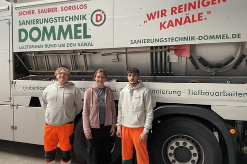 Drei Personen stehen vor einem Fahrzeug der Firma Dommel mit einem großen Werbeslogan zur Kanalsanierung.