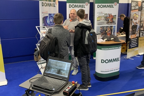Mitarbeiter von Dommel erklärt Besuchern eine Technologie an einem Messgerät mit Laptop auf einem Stand.