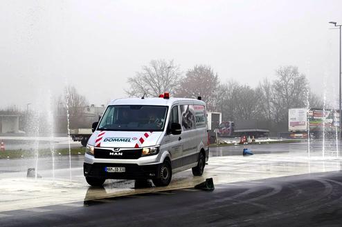 Ein MAN-Transporter fährt auf einer feuchten Verkehrsübungsfläche, während Spritzwasserfontänen aktiv sind.