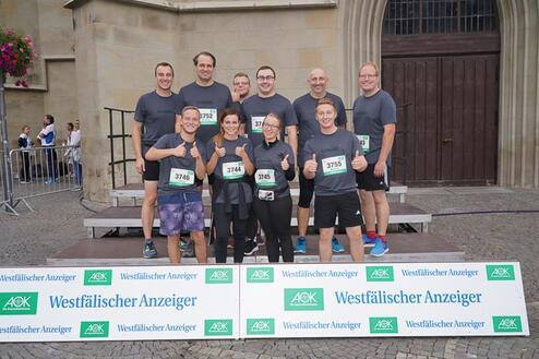 Gruppenfoto von zehn Teilnehmern in sportlicher Kleidung, die vor einem Banner des Westfälischen Anzeigers lächeln und Daumen hoch zeigen.
