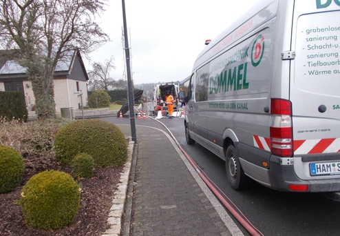 Blick auf einen Servicewagen der Firma Dommel, mit Arbeitern im Hintergrund, die ein Kanalreparaturprojekt durchführen.