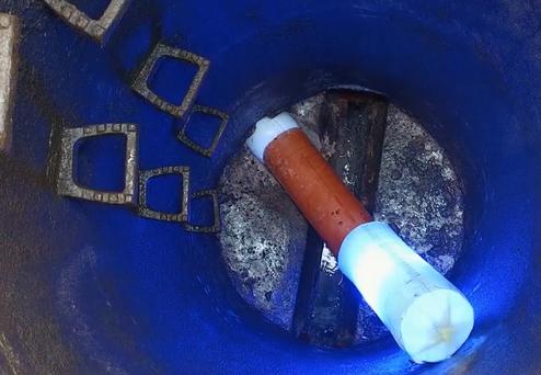 Blick in einen blauen Behälter mit einem orangefarbenen Rohr und mehreren quadratischen Metallstücken am Boden.