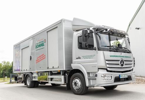 Silberner Transporter der Firma Dommel mit geöffneter Ladefläche auf einem gepflasterten Parkplatz.