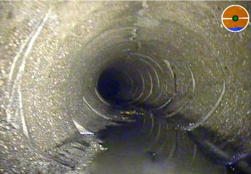 Blick in einen schmutzigen Abwasserkanal mit steinigen Wänden und stillstehendem Wasser am Boden.