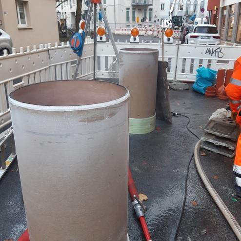 Zwei große zylindrische Rohre stehen auf einer Baustelle, umgeben von Bauzäunen und Werkzeugen.