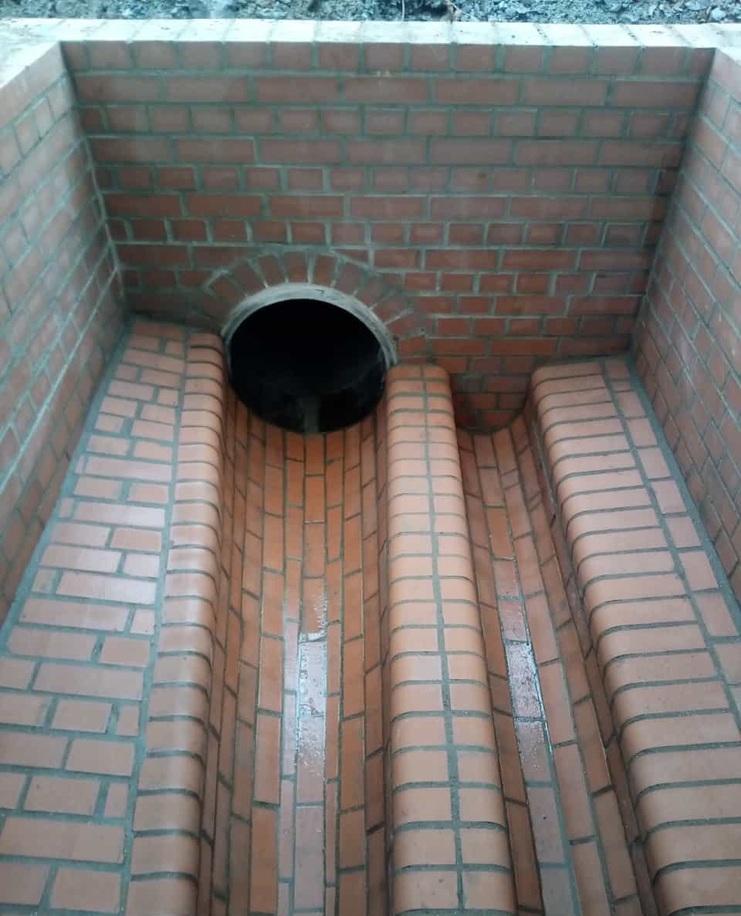 Treppenstufen aus roten Ziegeln führen zu einem runden Tunnel in einem gemauerten Raum.