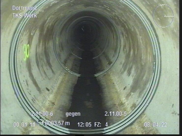 Innenansicht eines großen Abwasserrohrs mit Wasseransammlung in der Mitte und schlammigen Wänden.