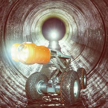 Roboter mit Scheinwerfer fährt in einem großen, runden Abwasserrohr durch das Wasser.