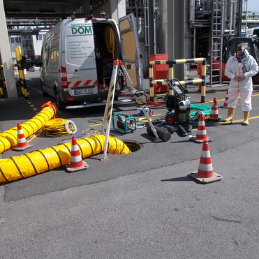 Arbeitsplatz mit Durchführung von Sanierungsarbeiten, auffallenden Warnkegeln und Ausrüstung um einen offenen Kanalschacht.