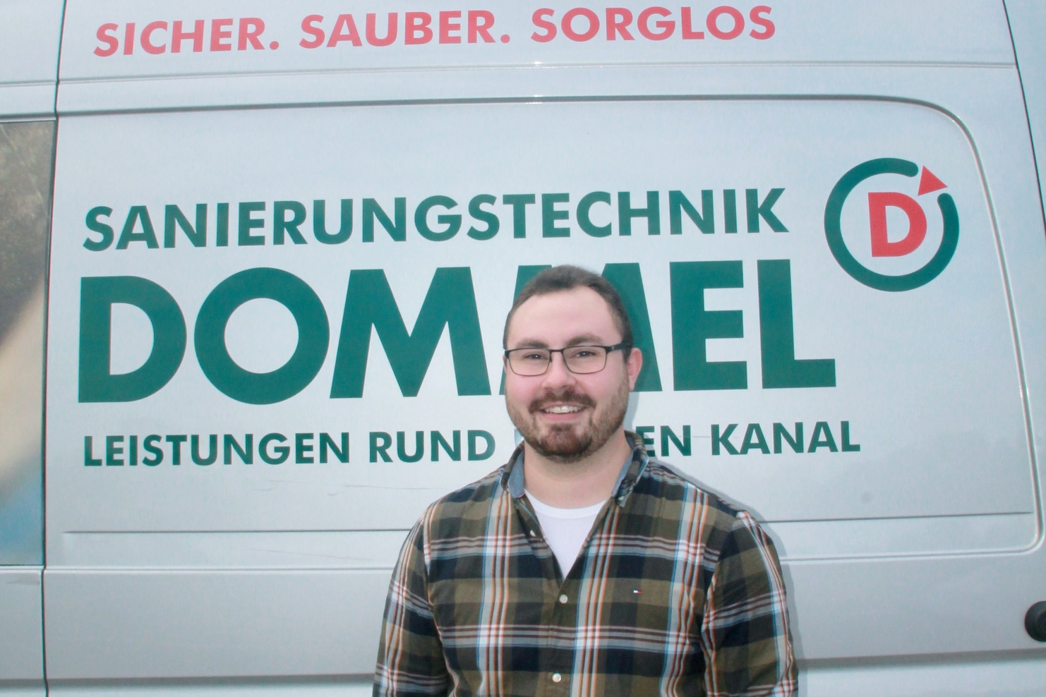Mann mit Brille steht vor einem Fahrzeug mit der Aufschrift „Sanierungstechnik Dommel“ und einem Slogan.