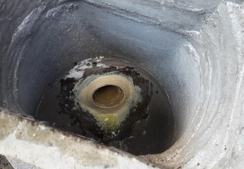 Blick ins Innere eines Gullys mit stehendem Wasser und Ablagerungen am Rand der runden Öffnung.