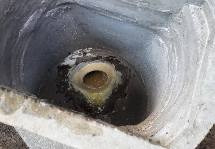 Blick ins Innere eines Gullys mit stehendem Wasser und Ablagerungen am Rand der runden Öffnung.