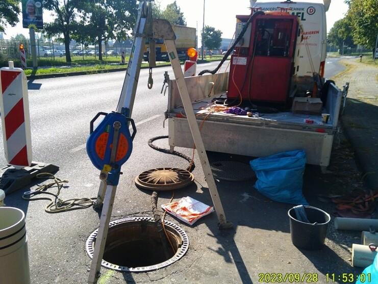 Bauarbeiten an einem Straßenkanal mit einem Abdeckungsrahmen, einem Kran und einem Servicefahrzeug im Hintergrund.