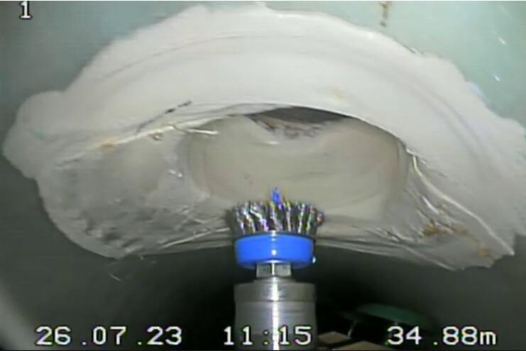 Nahaufnahme eines Rohraufsatzes mit Bürste, die auf eine Beschichtung in einem Rohr trifft.