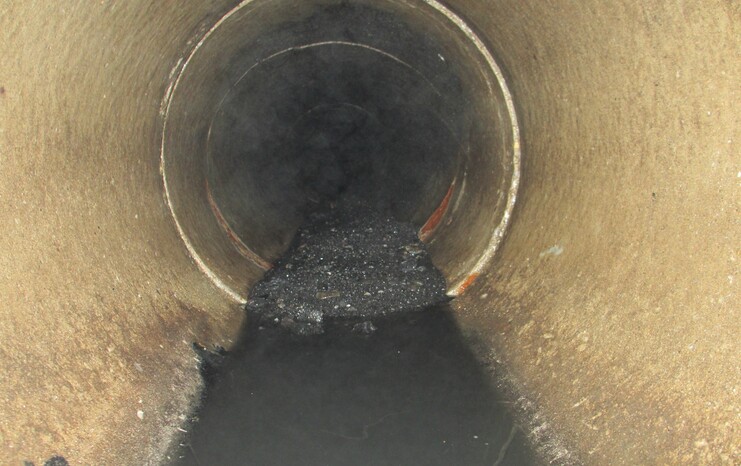 Blick in ein abgedunkeltes Rohr mit schwarzem Schmutz und stehendem Wasser am Boden.