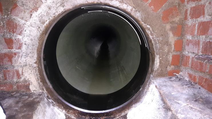 Runder, dunkler Abwasserkanal mit sichtbarem Wasser und ziegelsteinverkleideter Wand.