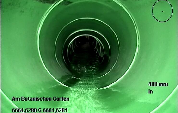 Blick in ein grünes Rohr mit fließendem Wasser, Sicht auf die Innenwand des Rohrs und Maßstab von 400 mm.