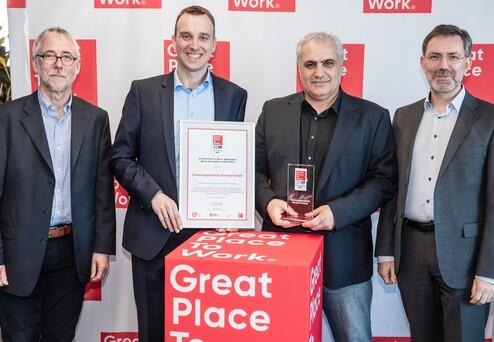 Vier Männer stehen neben einem Tisch mit einer Auszeichnung und einem Zertifikat für „Great Place to Work 2019“.