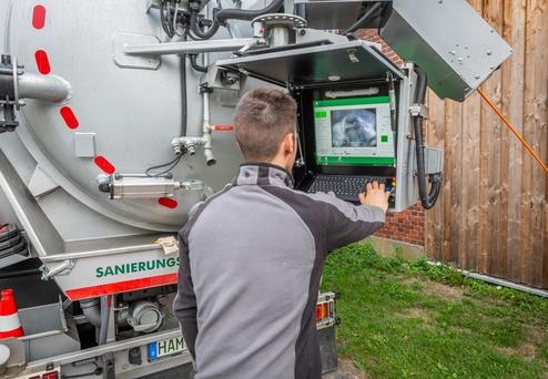 Mann bedient einen Computer an einem sanitären Fahrzeug mit Bildschirm und Kontrollpanel.