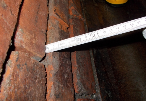 Messwerkzeug steht in einer Fuge zwischen roten Ziegelsteinen zur präzisen Vermessung.