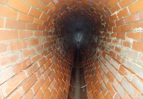 Blick in einen ziegelfurnierten Tunnel mit Wasserlauf in der Mitte, der in die Dunkelheit führt.