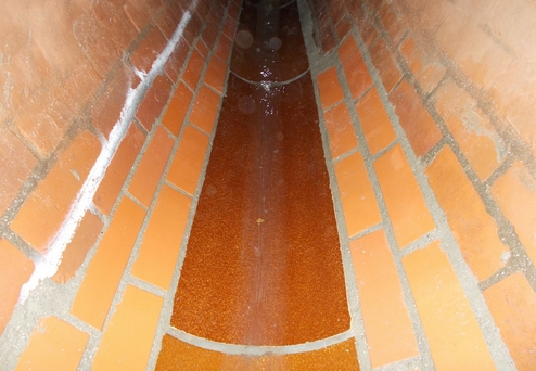 Blick in einen Ziegeltunnel mit wasserbeschichteter, brauner Fläche und orangefarbenen Klinkersteinen an den Wänden.
